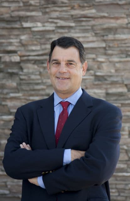 Dan Angress, a white man with dark brown hair wearing a blue business suit and smiling.