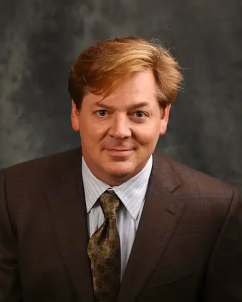 Dr. Gregory Henderson, a white man with reddish hair wearing a brown check suit.