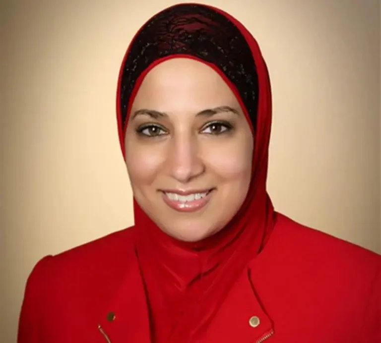 Dr. Mona Orady smiling wearing with a black lace and red head scarf and red suit.