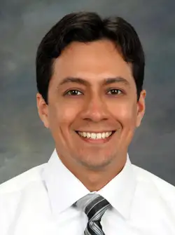 Dr. Aaron Dominguez, a smiling man with black hair in a button down shirt and tie.